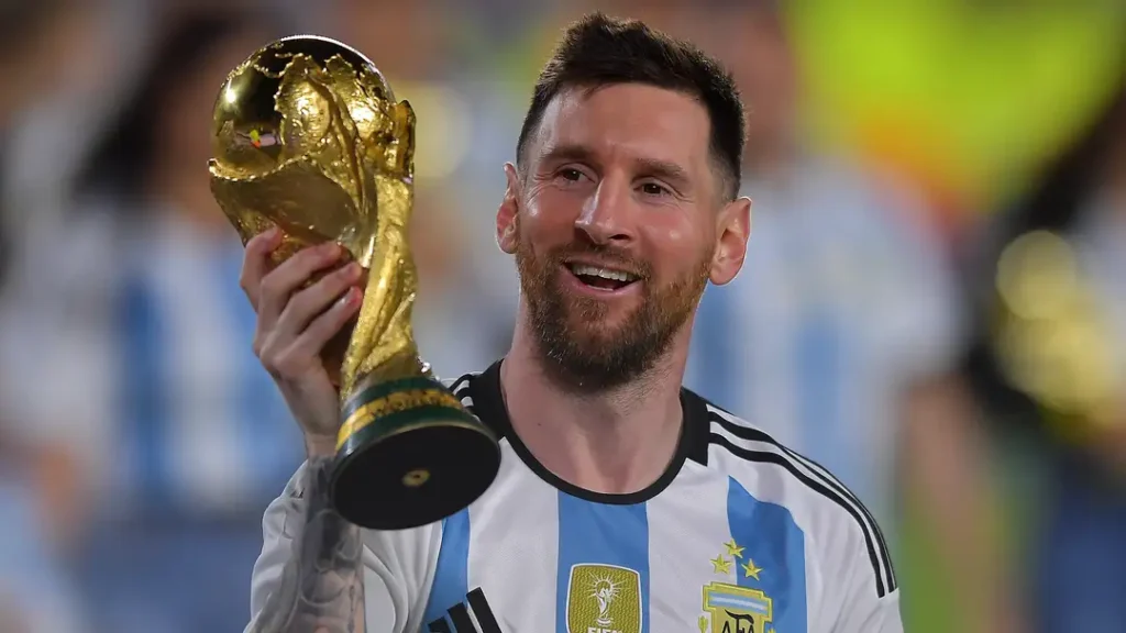 Messi Net Worth 2024: smiling while holding a football trophy.